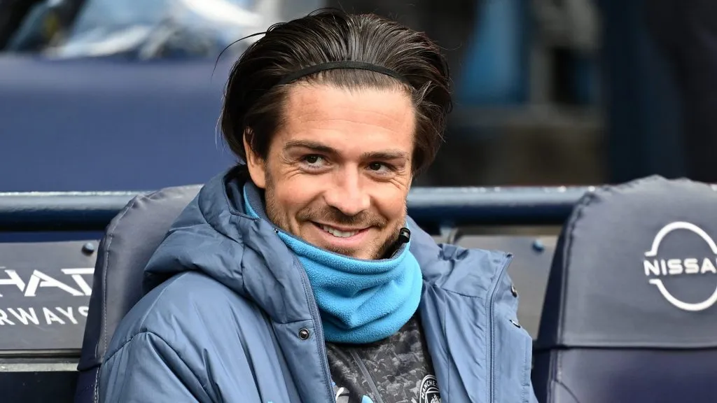 Grealish, ponta do Manchester City, sentado, com a jaqueta azul (Photo by Gareth Copley/Getty Images)
