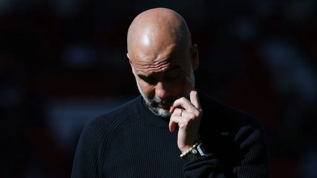 Guardiola, com a cabeça baixa, de blusa preta pelo Manchester City; (Photo by Michael Steele/Getty Images)