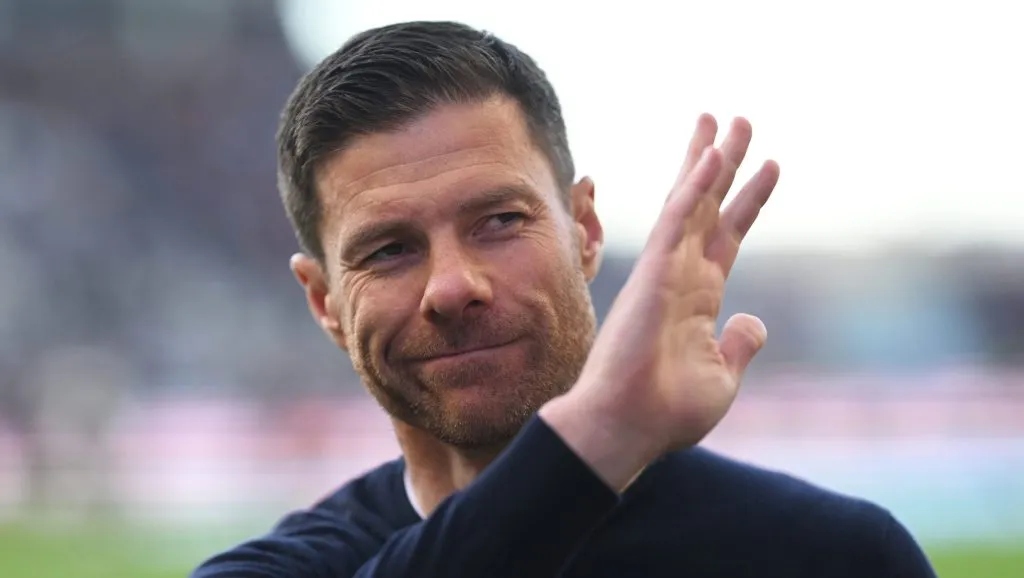 Xabi Alonso, em campo, com blusa preta e acenando com a mão
