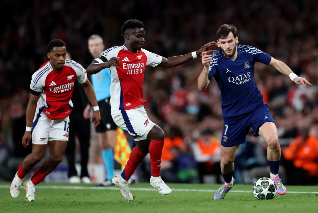 Khvicha Kvaratskhelia, do Paris Saint-Germain, conduz a bola enquanto é pressionado por Bukayo Saka, do Arsenal, durante a partida de ida da semifinal da UEFA Champions League 2024/25 entre Arsenal FC e Paris Saint-Germain, no Emirates Stadium, em 29 de abril de 2025, em Londres, Inglaterra. (Foto de Michael Steele/Getty Images)