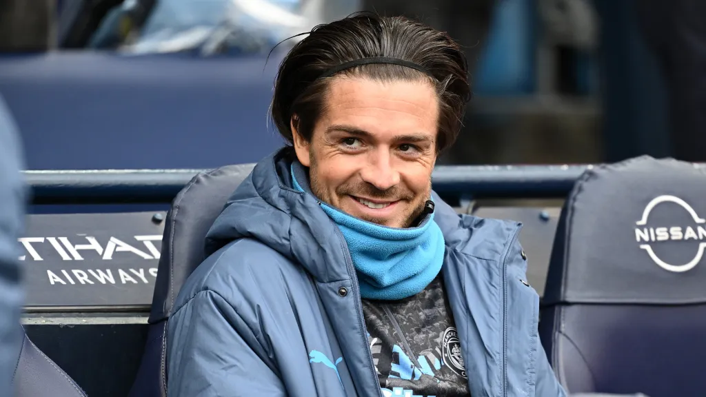 Jack Grealish sorrindo no banco de reservas do Manchester City (Foto: Gareth Copley/Getty Images)