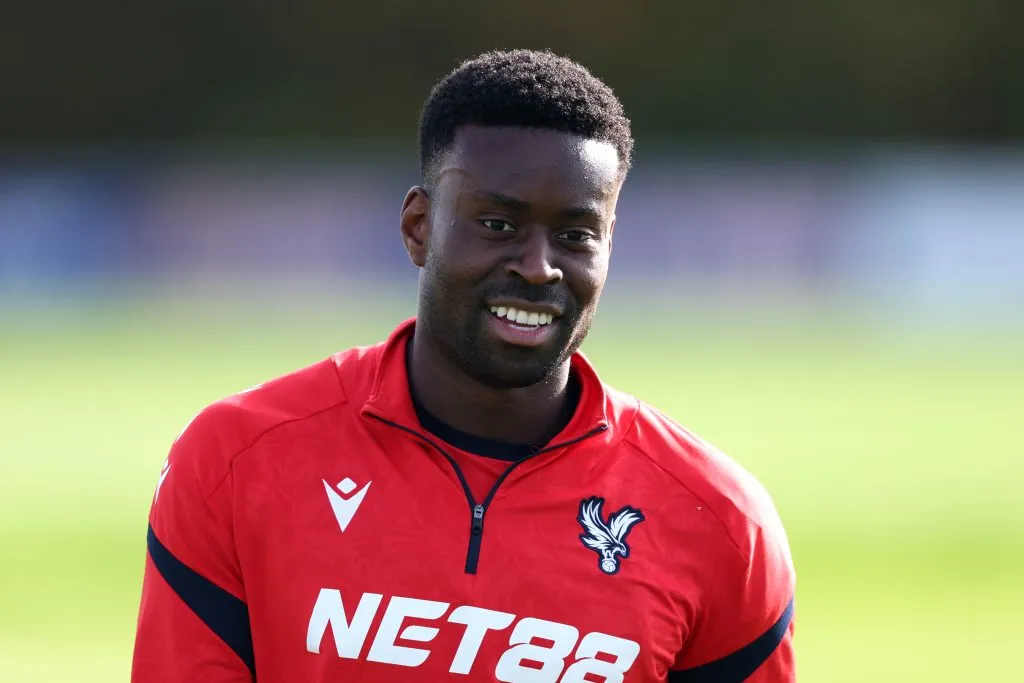 Marc Guéhi sorri usando um uniforme de treino do Crystal Palace na cor vermelha