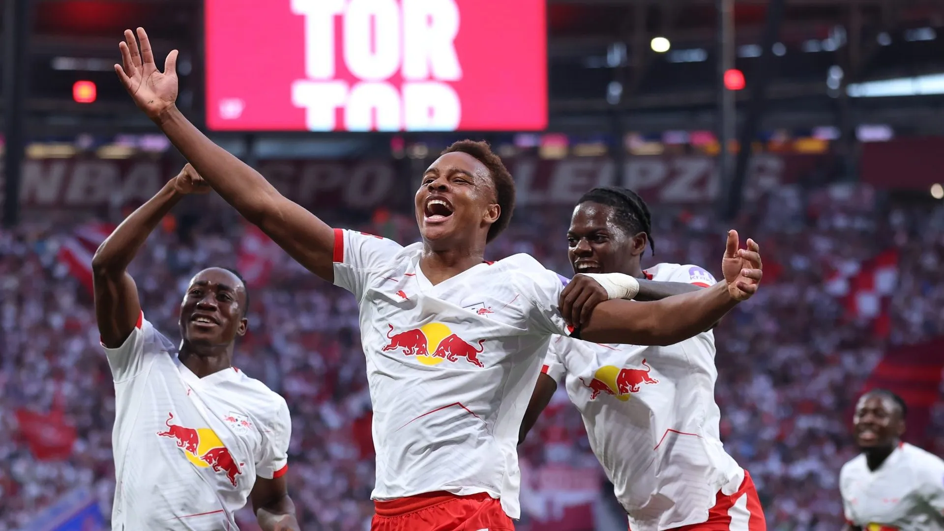 Assan Ouedraogo, do RB Leipzig, comemora o primeiro gol de sua equipe com os companheiros Yan Diomande (E) e Castello Lukeba (D) durante a partida da Bundesliga entre RB Leipzig e 1. FC Köln, na Red Bull Arena, em 20 de setembro de 2025, em Leipzig, Alemanha. (Foto: Maja Hitij/Getty Images)