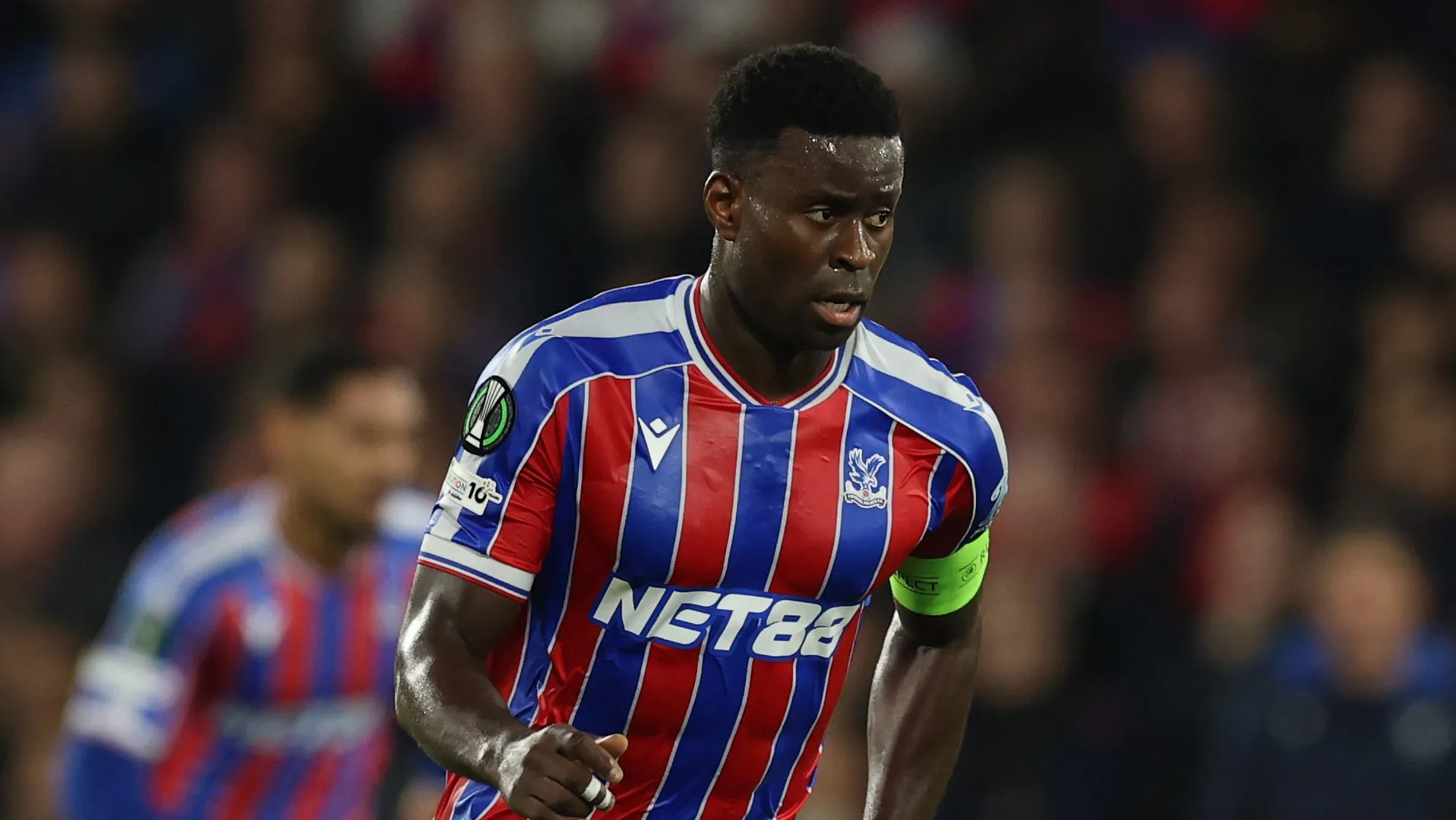 Marc Guéhi em movimento com a camisa usando a camisa azul e vermelha do Crystal Palace