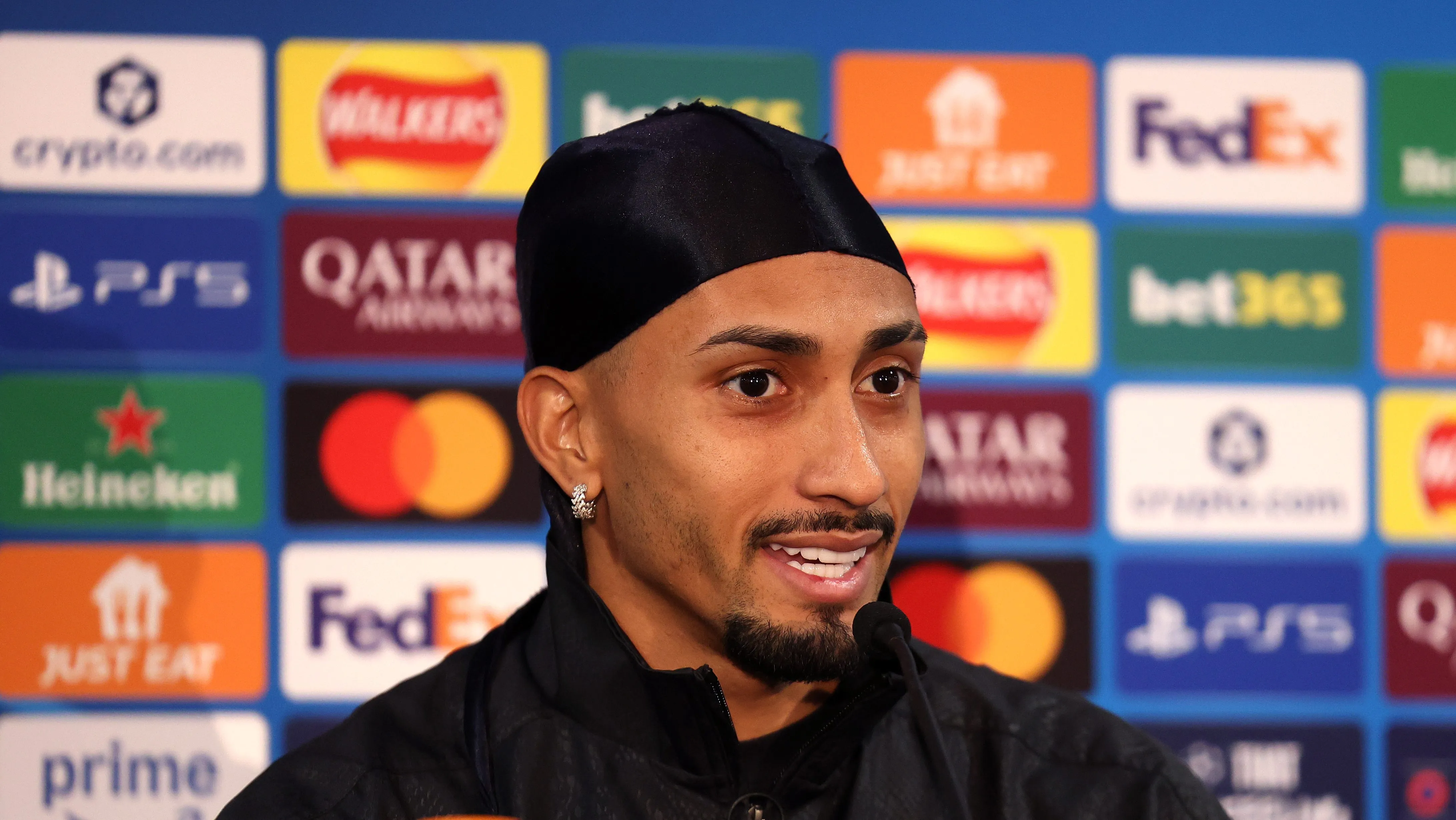 Raphinha em entrevista coletiva; jogador está usando uma espécie de bandana na cabeça