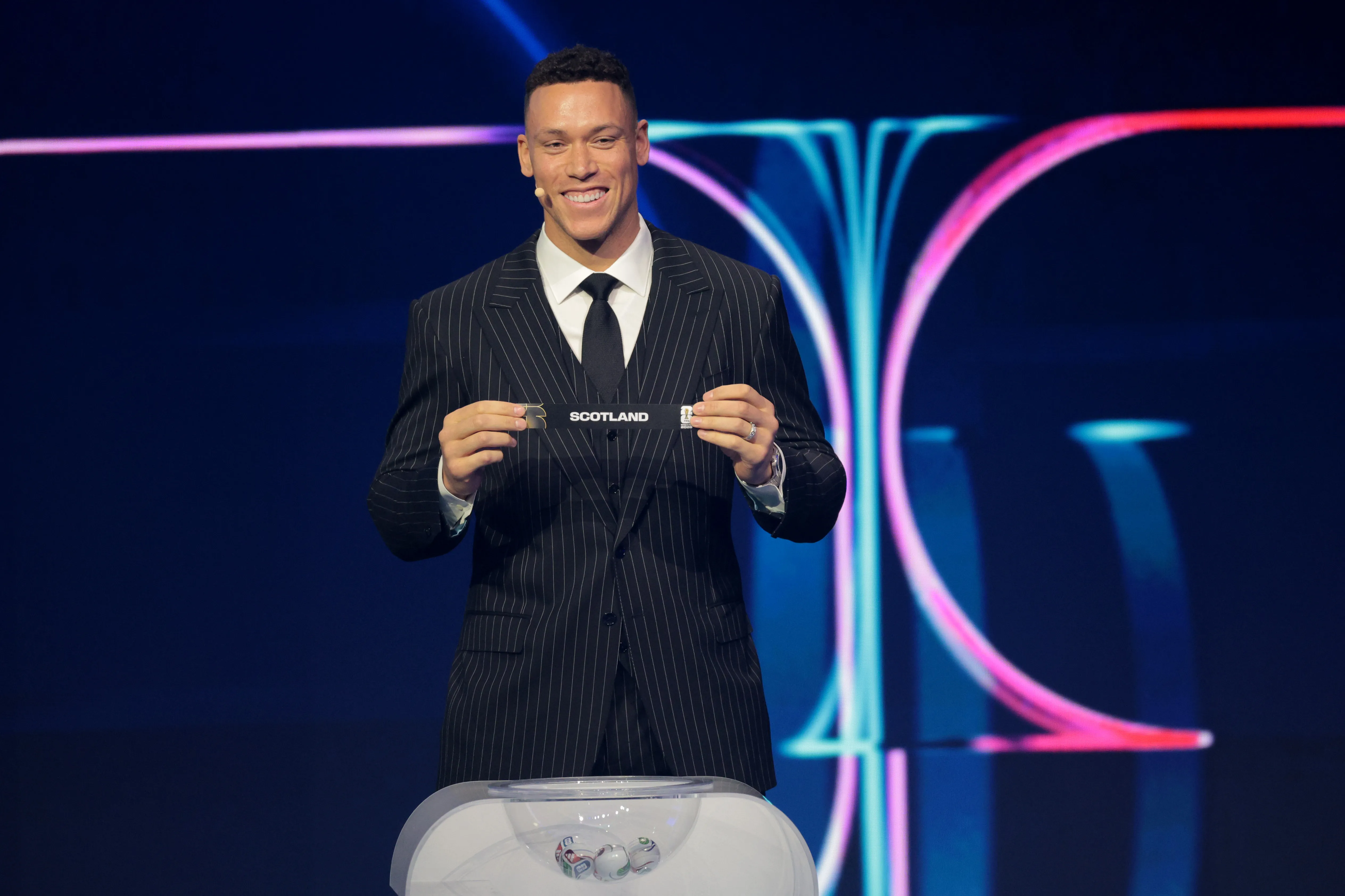 O assistente do sorteio Aaron Judge retira o cartão da Escócia durante o Sorteio Oficial da Copa do Mundo FIFA 2026, realizado no John F. Kennedy Center for the Performing Arts, em 05 de dezembro de 2025, em Washington, DC. (Foto: Kevin Dietsch/Getty Images)