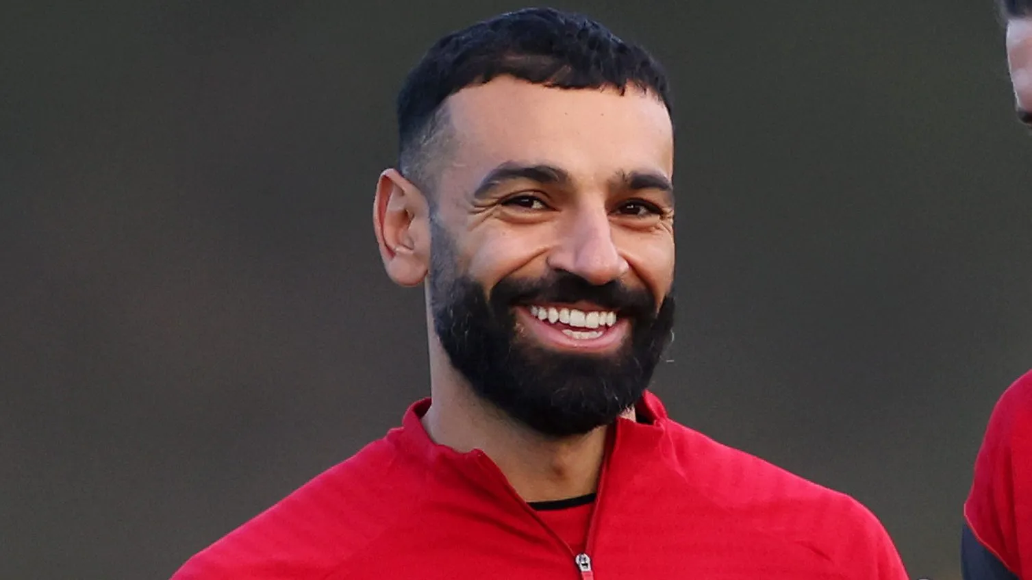 Mohamed Salah em campo, sorrindo, de camisa vermelha do Liverpool