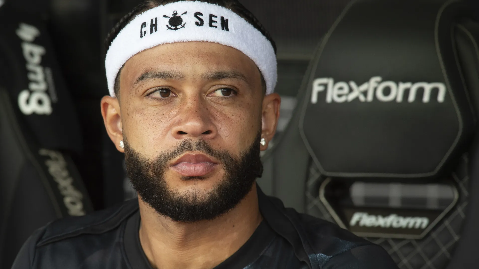 Memphis Depay aparece, no banco, olhando para o centro durante um jogo pelo Corinthians