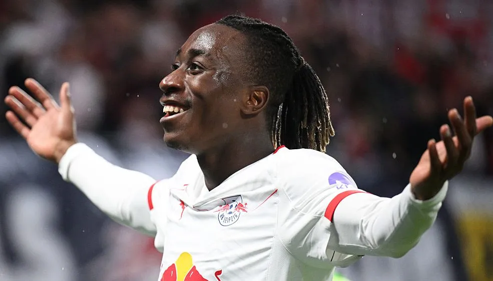 Yan Diomande, do RB Leipzig, em campo, com os braços abertos comemorando. Jogador é alvo do Arsenal