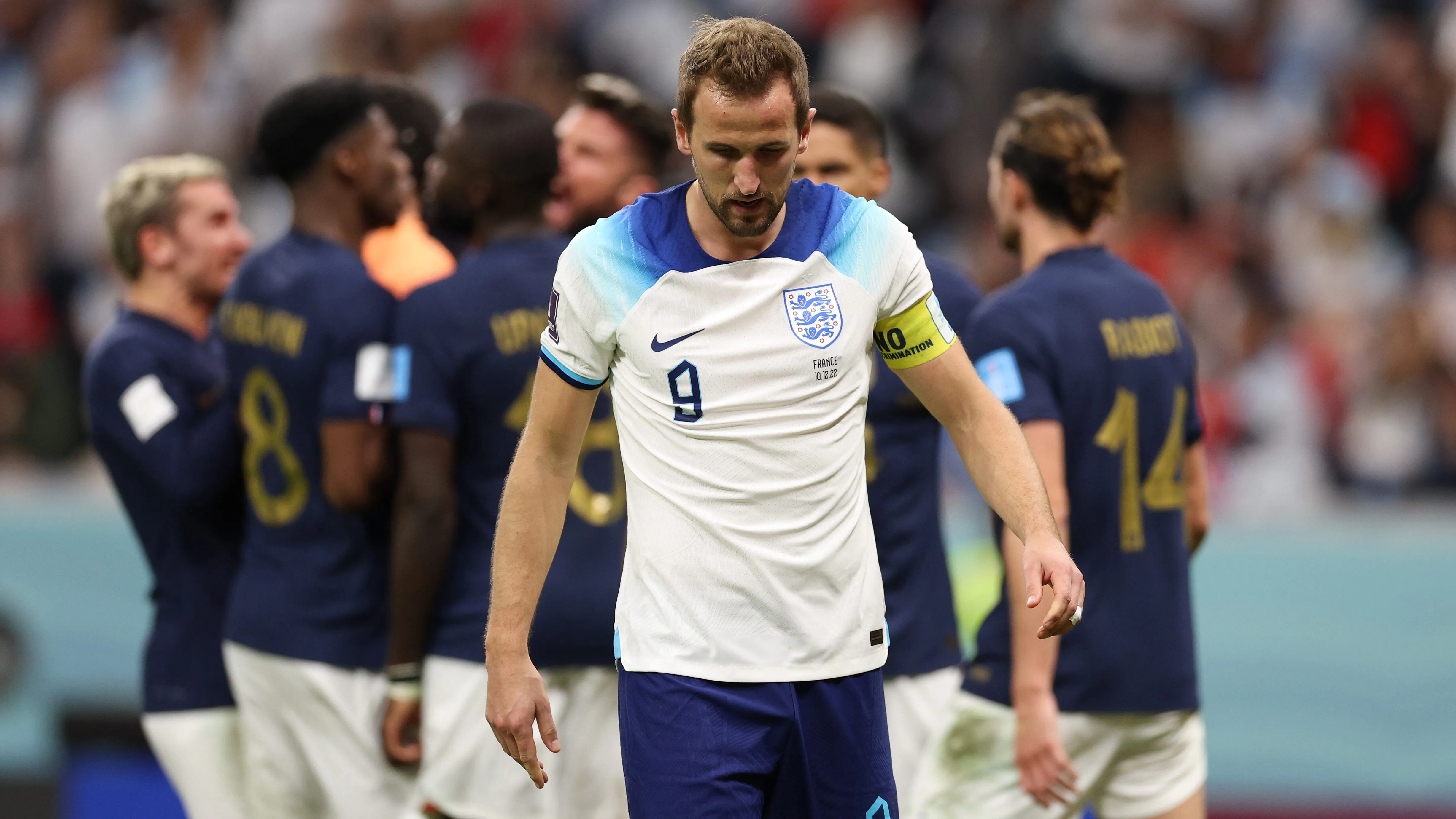 Harry Kane cabisbaixo em jogo da Inglaterra e jogadores da frança comemoram no fundo da imagem